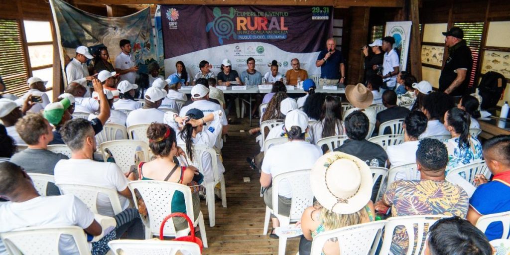 Un grupo de más de 20 personas sentadas en sillas ponen atención a los panelistas del encuentro de jóvenes rurales en Nuquí, Chocó, rumbo a la COP16.