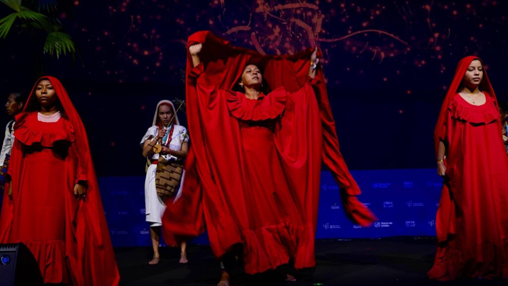 Ensayo del acto inaugural de la COP16, se ve a tres mujeres con trates rojos típicos realizando un performance.