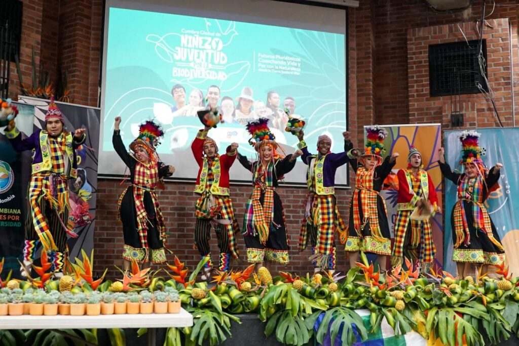 Jóvenes bailando sobre una tarima vestidos con trajes típicos durante la Cumbre Global de Niñez y Juventud en el marco de la COP16.