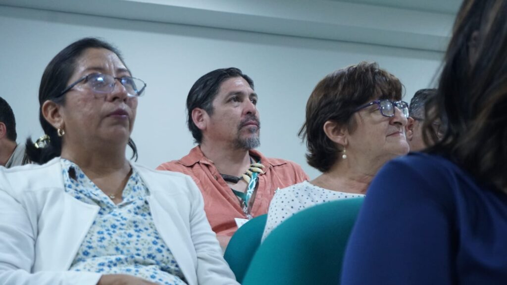 Tres personas observando de manera atenta hacia al frente del auditorio, dos mujeres y un hombre, muy atentos a lo que está sucediendo en el atrio, en el evento Conectividad del Pacìfico Oriental: Clave para la Conservaciòn Global en la COP16.